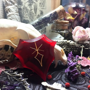 May include: A red, star-shaped resin pendant with a gold-colored design. The pendant is surrounded by dried flowers and other natural elements.