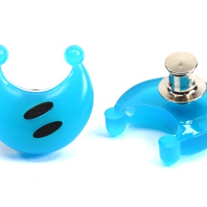 May include: Two blue crescent moon shaped plastic buttons with black eyes. One button has a silver pin on the back.
