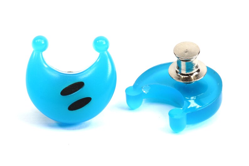 May include: Two blue crescent moon shaped plastic buttons with black eyes. One button has a silver pin on the back.