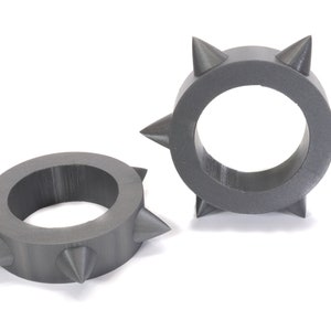 May include: Two grey, 3D printed rings with sharp, pointed spikes around the circumference.