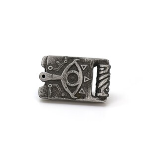 May include: A silver-colored metal charm with a detailed design of an eye with a triangle pattern and circuitry. The charm has a small hole at the top for attaching to a necklace or bracelet.