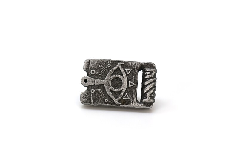 May include: A silver-colored metal charm with a detailed design of an eye with a triangle pattern and circuitry. The charm has a small hole at the top for attaching to a necklace or bracelet.