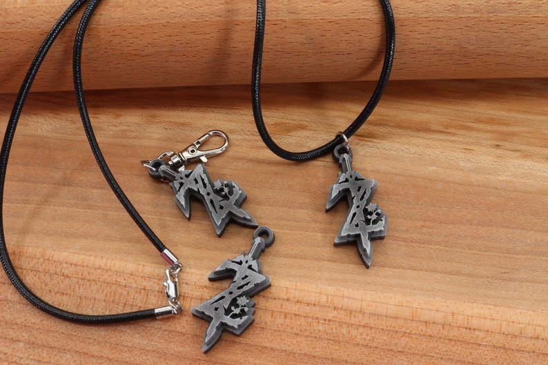 May include: Three silver pendants with a stylized design, two on black cords and one on a silver chain. The pendants are in the shape of a sword with a stylized design.