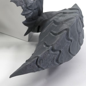Op de afbeelding: Een grijze, getextureerde, 3D-geprinte drakenstaart met scherpe, puntige randen.