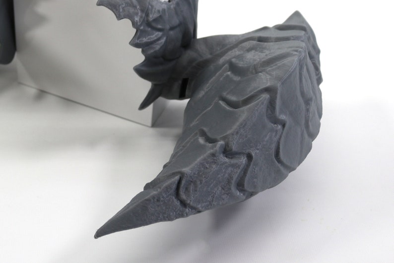 Op de afbeelding: Een grijze, getextureerde, 3D-geprinte drakenstaart met scherpe, puntige randen.