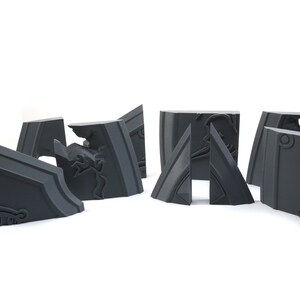 May include: A set of six gray, intricately detailed, 3D printed puzzle pieces. The pieces are shaped like geometric blocks with a variety of angles and curves. The pieces are designed to fit together to form a larger structure.