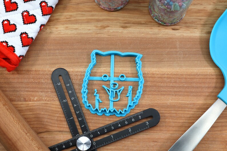 May include: A blue plastic cookie cutter shaped like a dog's head. The cutter has a detailed design with a tongue sticking out.