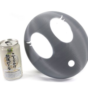 May include: A gray plastic disc with two oval-shaped cutouts and a smaller round cutout. The disc is next to a can of Japanese beer.