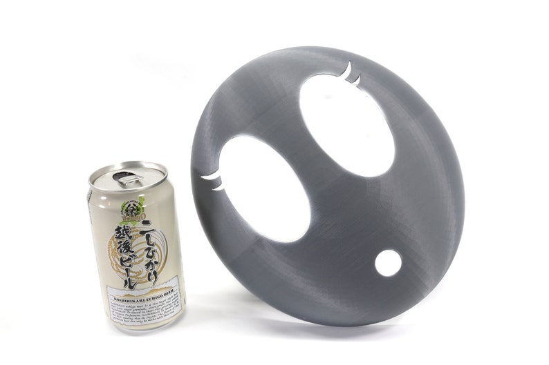 May include: A gray plastic disc with two oval-shaped cutouts and a smaller round cutout. The disc is next to a can of Japanese beer.