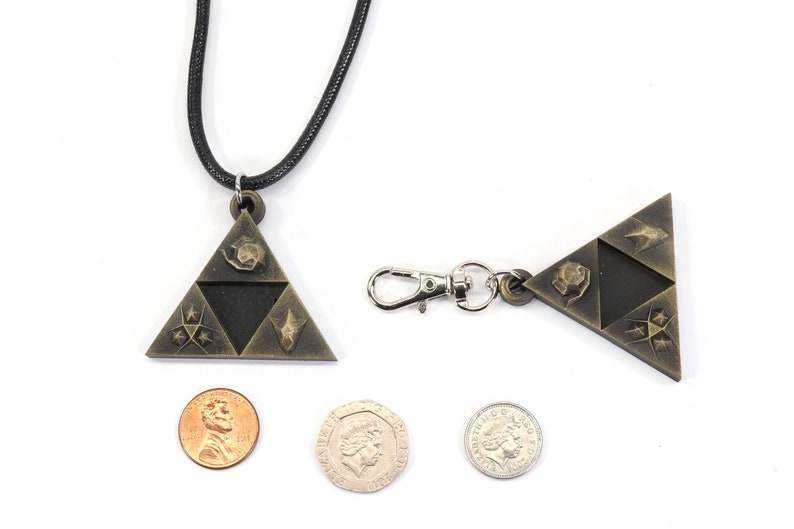 May include: A gold-colored pendant necklace featuring a triangular design with four symbols. The pendant is about the size of a US quarter. The necklace is on a black cord. There is also a matching keychain with a silver clasp.