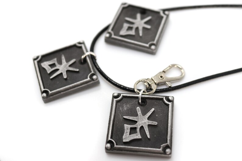 May include: A black necklace with three silver square pendants. Each pendant has a silver kanji character on a black background.
