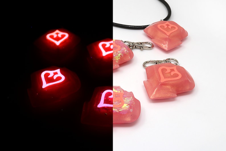 May include: Four pink resin keycaps with a white heart design. The keycaps glow pink in the dark. One keycap is attached to a black cord and two silver keychains.