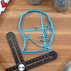 May include: A blue plastic cookie cutter shaped like a human head with lines for eyes, nose, and mouth.
