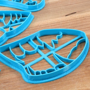 May include: A set of four blue plastic cookie cutters shaped like leaves. The cutters are on a wooden surface.