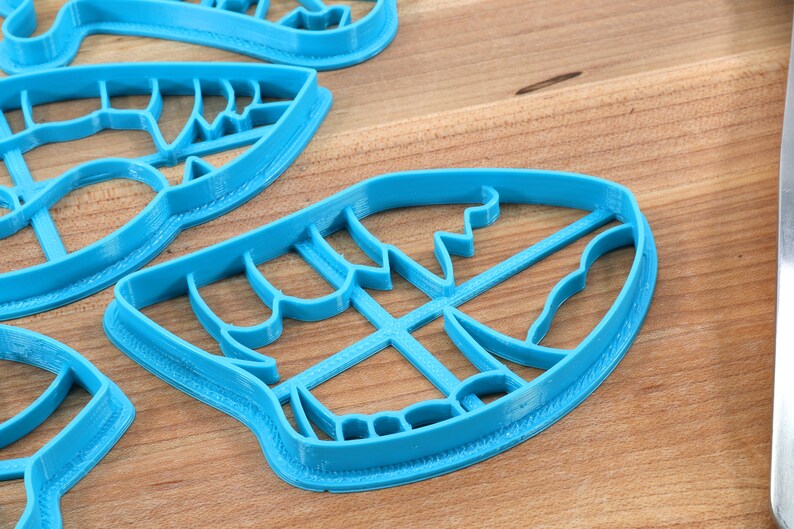 May include: A set of four blue plastic cookie cutters shaped like leaves. The cutters are on a wooden surface.
