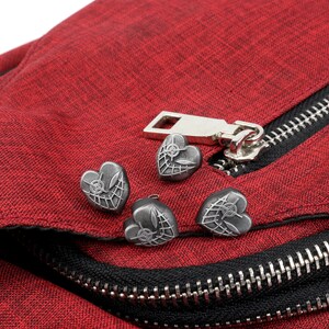 May include: Close-up of a red fabric bag with a black zipper and four silver heart-shaped zipper pulls. Each heart has a web design.