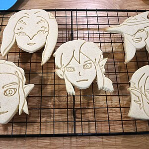 May include: Four sugar cookies decorated with an outline of a cartoon face. The cookies are on a black wire cooling rack.