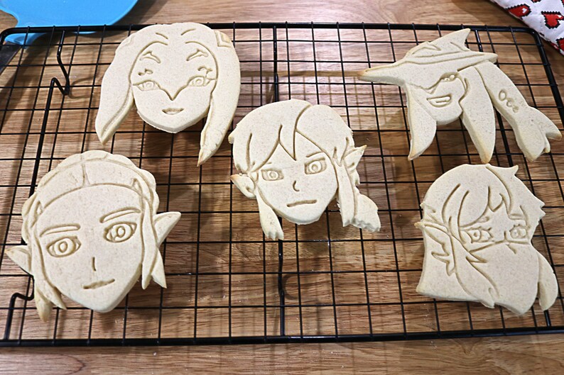 May include: Four sugar cookies decorated with an outline of a cartoon face. The cookies are on a black wire cooling rack.