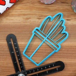 K&ouml;nnte beinhalten: Ein blauer Plastik-Ausstecher in Form einer Topfpflanze. Der Ausstecher hat ein detailliertes Design mit mehreren Bl&auml;ttern und einem Topf.