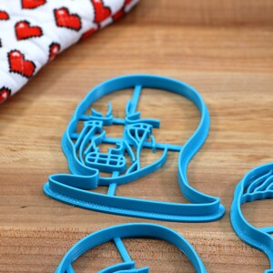 Op de afbeelding: Drie blauwe plastic koekjesvormen in de vorm van gezichten. De vormen liggen op een houten oppervlak.