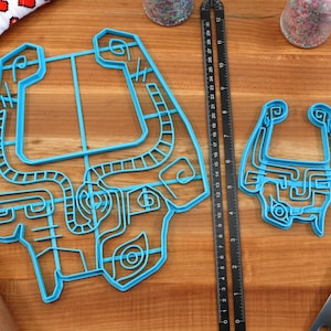 Peut inclure: Deux emportes-pi&egrave;ces en plastique bleu en forme de Triforce de la s&eacute;rie de jeux vid&eacute;o The Legend of Zelda. Le plus grand emporte-pi&egrave;ce mesure environ 15 cm de large et le plus petit environ 7,5 cm de large. Les emportes-pi&egrave;ces sont sur une surface en bois.