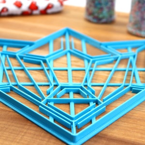 Puede incluir: Un cortador de galletas geom&eacute;trico de pl&aacute;stico azul con forma de estrella. El cortador est&aacute; hecho de m&uacute;ltiples capas de pl&aacute;stico, creando un efecto 3D.