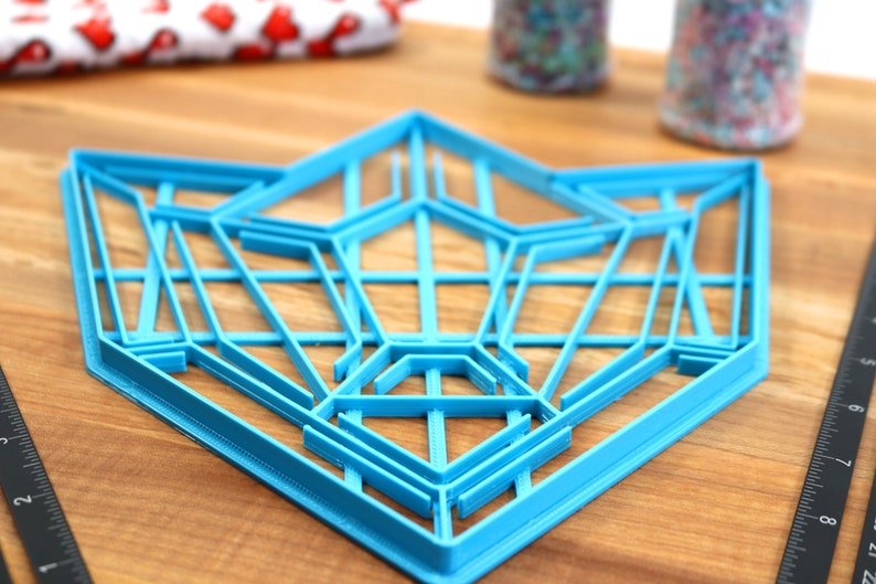 Puede incluir: Un cortador de galletas geom&eacute;trico de pl&aacute;stico azul con forma de estrella. El cortador est&aacute; hecho de m&uacute;ltiples capas de pl&aacute;stico, creando un efecto 3D.