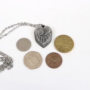 May include: A silver heart-shaped pendant necklace with a detailed design, displayed with five coins of different denominations.