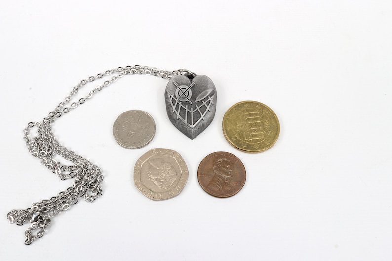 May include: A silver heart-shaped pendant necklace with a detailed design, displayed with five coins of different denominations.