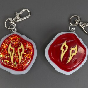 May include: Two red and white resin keyrings with a gold flame design. The keyrings have a silver metal loop.