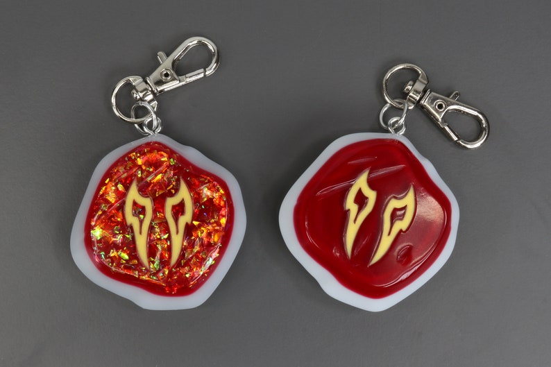 May include: Two red and white resin keyrings with a gold flame design. The keyrings have a silver metal loop.