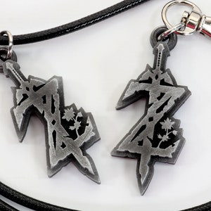 May include: Two silver-colored pendants featuring a stylized sword design with a floral motif. One pendant is attached to a black cord necklace, while the other is attached to a silver key chain.