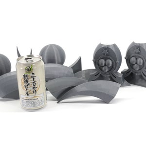 May include: A gray 3D printed model of a robot with a can of Japanese beer in the foreground. The robot has a star on its chest and a circular design on its head. The beer can has Japanese text and the words "Japanese Craft Liquor" printed on it.