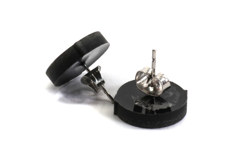 May include: A pair of black stud earrings with silver posts and backs. The earrings are round and have a smooth, polished finish.