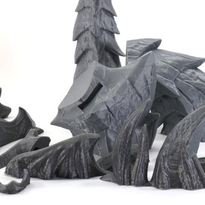 May include: A set of gray 3D printed miniature terrain pieces for tabletop gaming. The set includes a variety of shapes, including trees, rocks, and spikes.