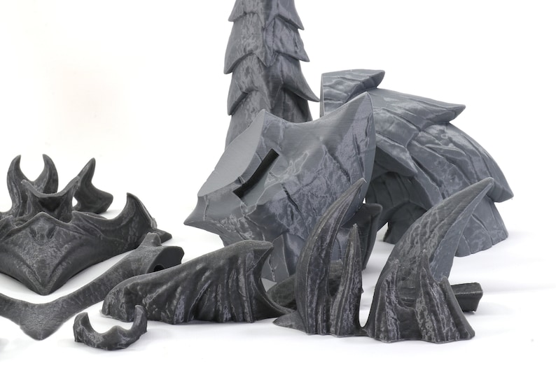 May include: A set of gray 3D printed miniature terrain pieces for tabletop gaming. The set includes a variety of shapes, including trees, rocks, and spikes.