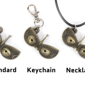 May include: Three versions of a gold-colored metal pendant shaped like a pair of eyes with a small antenna. The pendant is shown as a standard piece, a keychain, and a necklace.