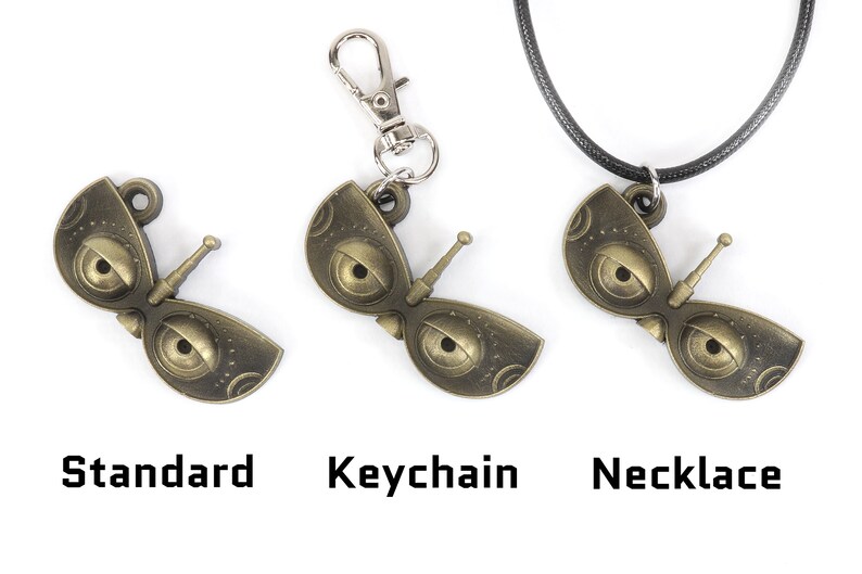 May include: Three versions of a gold-colored metal pendant shaped like a pair of eyes with a small antenna. The pendant is shown as a standard piece, a keychain, and a necklace.