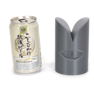 May include: A silver can of Japanese beer with the text "こしひかり 越後" (Koshihikari Echigo) and a grey 3D printed object shaped like a stylised eye.