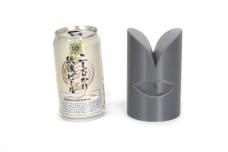 May include: A silver can of Japanese beer with the text "こしひかり 越後" (Koshihikari Echigo) and a grey 3D printed object shaped like a stylised eye.