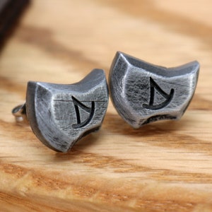 May include: A pair of silver earrings with a textured finish and a symbol engraved on each. The symbol is a stylized letter 'Y' with a curved line.