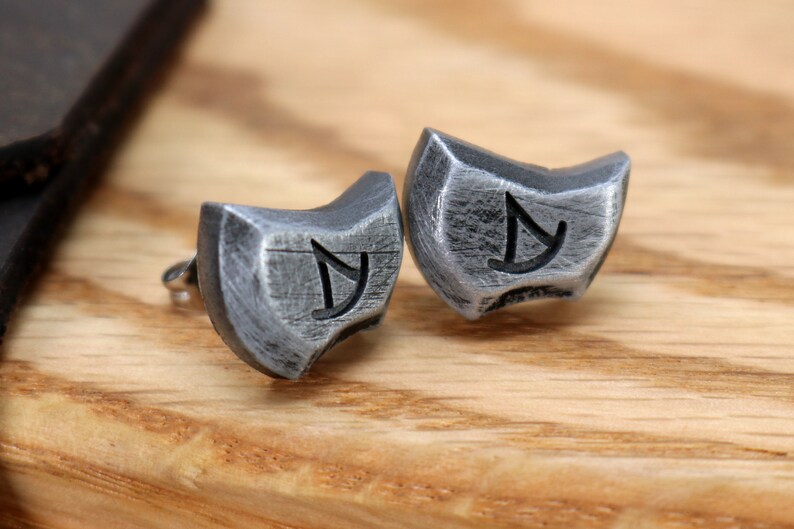 May include: A pair of silver earrings with a textured finish and a symbol engraved on each. The symbol is a stylized letter 'Y' with a curved line.