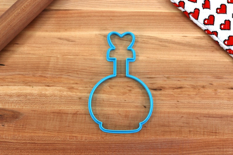 May include: Blue plastic cookie cutter shaped like a bottle with a heart-shaped top.