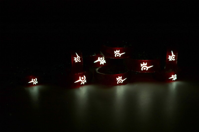 May include: A group of red glow-in-the-dark rings with a white symbol on each ring. The symbol is a stylized design of a crown with a point.