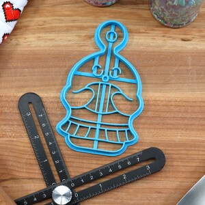 May include: A blue plastic cookie cutter shaped like a skull with a top hat. The cookie cutter is on a wooden surface.