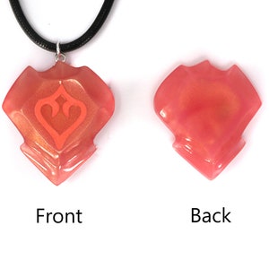 May include: A coral-colored pendant necklace with a geometric design and a smaller heart-shaped design inside. The pendant is made of resin and has a glossy finish. The necklace is on a black cord.