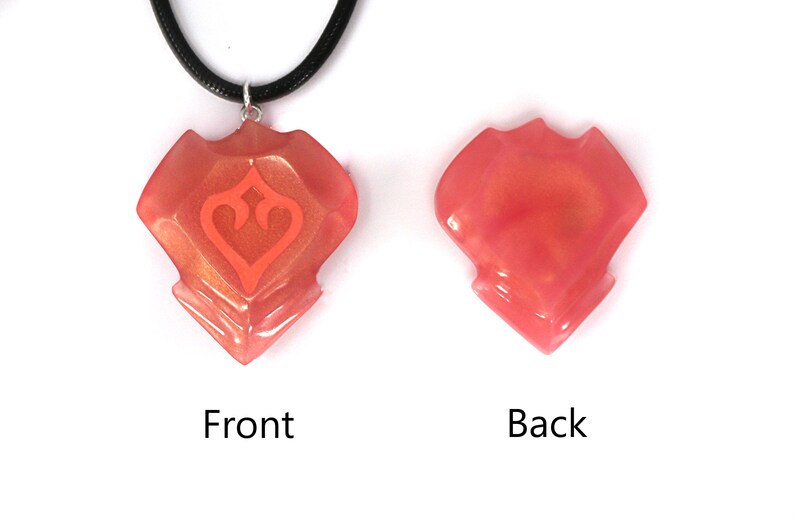 May include: A coral-colored pendant necklace with a geometric design and a smaller heart-shaped design inside. The pendant is made of resin and has a glossy finish. The necklace is on a black cord.