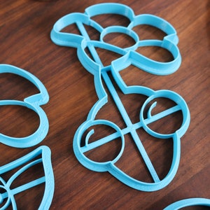 May include: A set of three blue plastic cookie cutters shaped like flowers. The cutters are on a wooden surface.