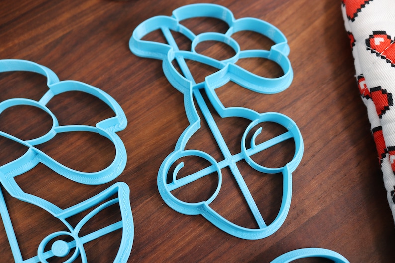 May include: A set of three blue plastic cookie cutters shaped like flowers. The cutters are on a wooden surface.