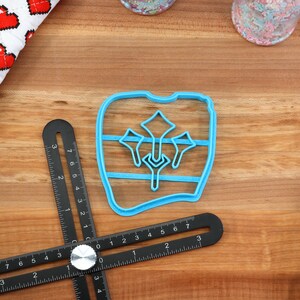 May include: A blue plastic cookie cutter shaped like a tooth with a design of three stylized flowers inside. The cutter is on a wooden surface.